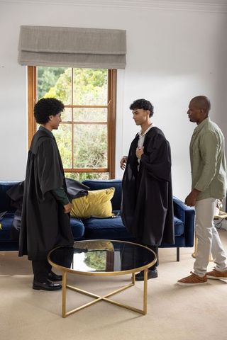 Multicultural family celebrating home graduation with two young men wearing black academic gowns