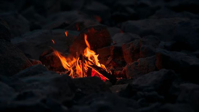 Glowing campfire in rocky ring at night with flickering flames, embers and sparks