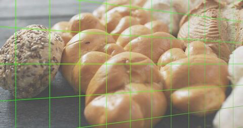 Braided challah loaf with seeded roll on dark wood surface with green grid overlay