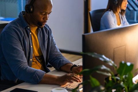 African american agent typing on white keyboard with headset in modern open-plan office