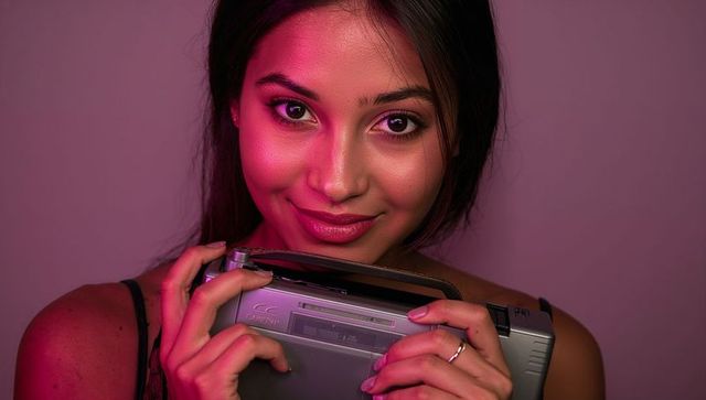 Smiling young woman holding portable cassette player with magenta lighting and retro vibe
