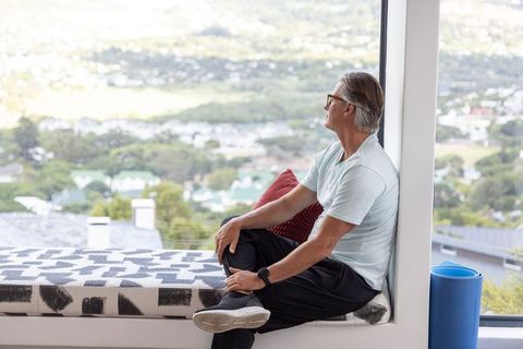 Mature man sitting on window bench gazing at panoramic city view