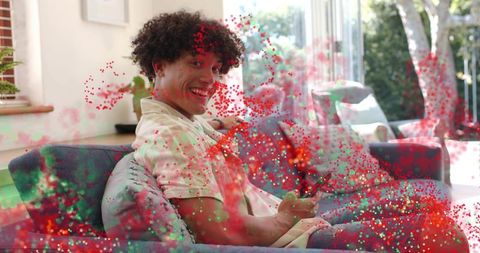 Smiling man relaxing on blue sofa holding remote amid confetti in bright modern lounge