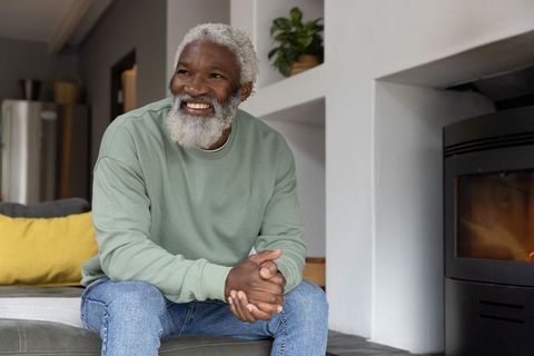 Senior african american man smiling and enjoying cozy warmth by wood-burning stove