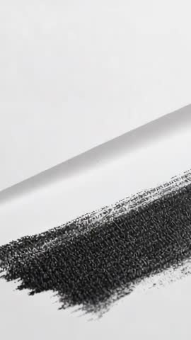 Revealing charcoal swatch sliding across folded paper, showing textured grain macro vertical