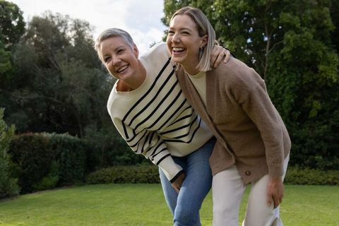 Mature women laughing and leaning together in sunlit backyard, joyful friendship moment