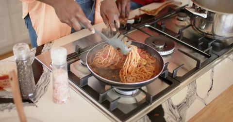 Cooking steaming spaghetti on gas stove stirring tomato pasta in nonstick pan lifting noodles