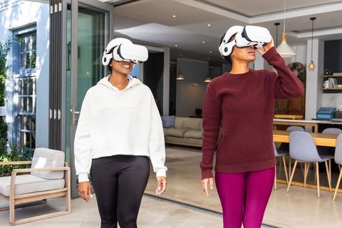 Diverse friends exploring virtual reality at home wearing white vr headsets in living area