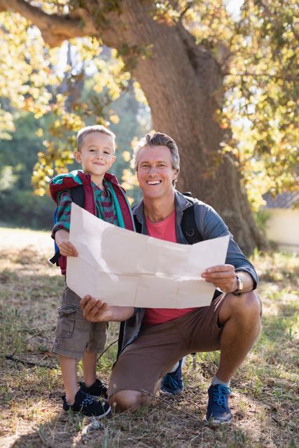 Father and son enjoying a day in the forest, holding a map and smiling. Perfect for themes of family bonding, outdoor activities, adventure, and nature exploration. Suitable for use in travel blogs, family-oriented advertisements, and educational materials about nature and outdoor activities.