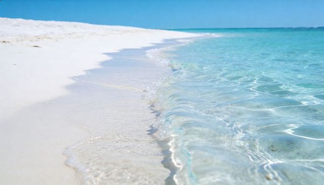 Lapping white sand beach showing transparent turquoise water and rippling sand reflections