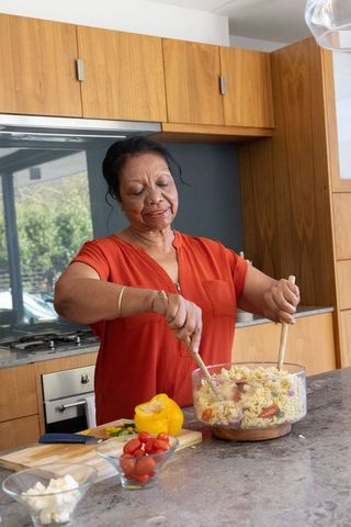 Senior african american woman stirring pasta salad in modern sunlit home kitchen