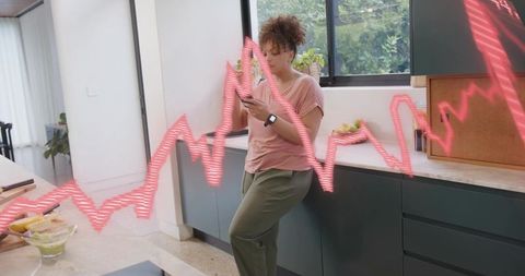 Young woman leaning in modern kitchen checking smartphone with smartwatch and digital waveform