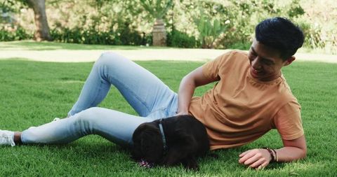 Young Man Relaxing on Lawn with Playful Puppy in Sunny Backyard