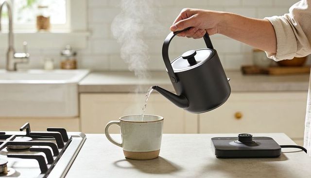 Pouring hot water from black gooseneck kettle into ceramic mug on kitchen counter
