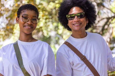 Sunlit couple smiling and posing outdoors in white tees with crossbody bags