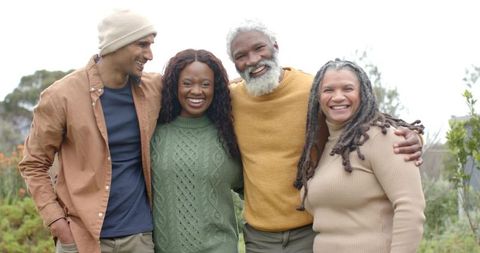 Smiling diverse friends embracing outdoors in knit sweaters and beanie