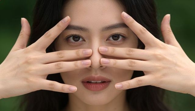 Closeup asian woman placing fingers across face natural makeup expressive beauty portrait