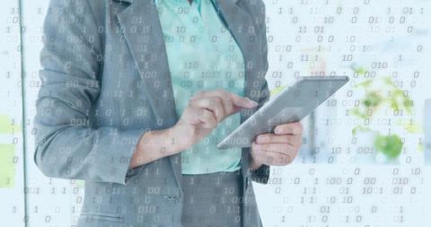 Businesswoman holding tablet tapping digital screen with binary code overlay in office