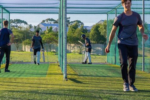 Cricket teammates practicing batting drills in outdoor net lanes wearing pads and helmets