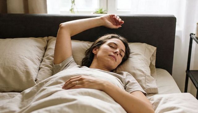 Woman resting peacefully in cozy neutral bedroom wearing ring with plants and soft linen