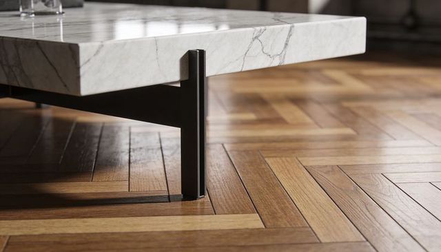 Minimal marble coffee table corner with black metal leg on herringbone parquet floor