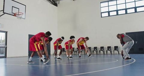 Diverse basketball team stretching on court with coach guidance