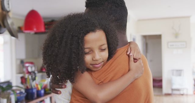 Smiling african american daughter hugging father in kitchen. Fatherhood, childhood, care, love, togetherness and domestic life.