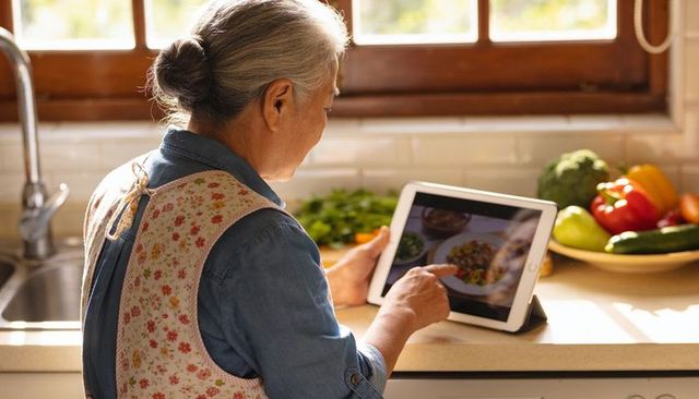 Senior woman following tablet recipe in sunny home kitchen with fresh vegetables