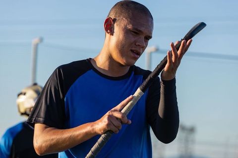 Hispanic male athlete evaluating hockey stick on field
