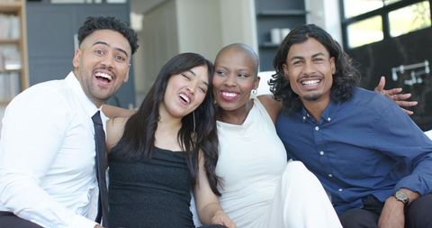 Diverse friends laughing on couch enjoying casual party in modern open-plan living room