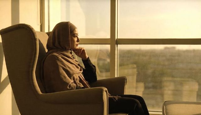 Sunlit contemplative woman in hijab gazing through lounge window at sunset