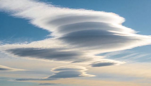 Stacking lenticular clouds forming layered lens shapes across clear blue sky at dawn