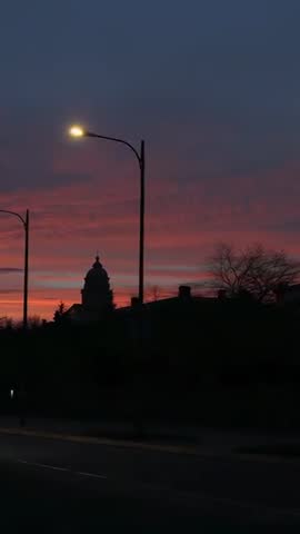 Vertical video capturing domed landmark silhouette at sunset with streetlights and passing car