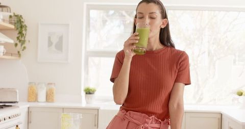 Woman sipping healthy green smoothie in bright minimalist kitchen