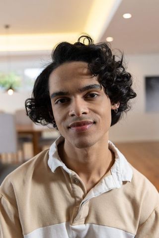 Young man with curly hair wearing rugby shirt and hoop earrings smiling in modern home