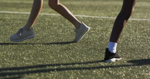 Diverse teen athletes running on sunlit turf field in sneakers and ankle socks