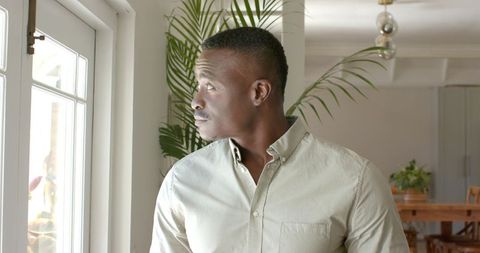 African American man standing by window looking thoughtful in modern home interior