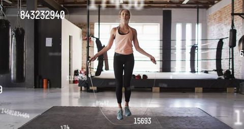 Female athlete jumping rope in boxing gym with fitness hud overlay for cardio training