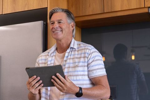 Mature man using tablet in modern kitchen smiling, relaxed lifestyle