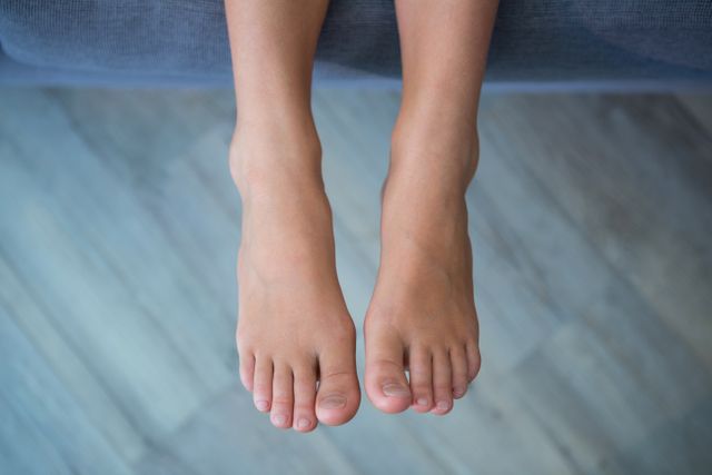 This image shows a girl's legs and feet from an overhead perspective while she is sitting on a sofa. It can be used in contexts related to relaxation, childhood, home life, and casual settings. Ideal for articles, blogs, or advertisements focusing on family life, comfort, or children's activities.