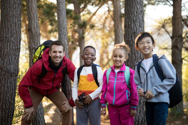 Teacher and diverse group of kids enjoying an outdoor adventure in a park on a sunny day. They are smiling and wearing backpacks, suggesting they are on a hike or nature exploration. This image can be used for educational materials, outdoor activity promotions, or articles about childhood development and outdoor learning.
