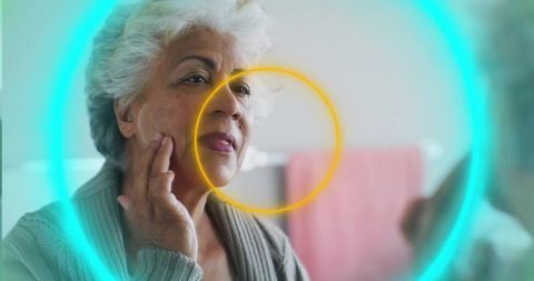 Senior woman examining skin in mirror with teal and yellow ring light accents
