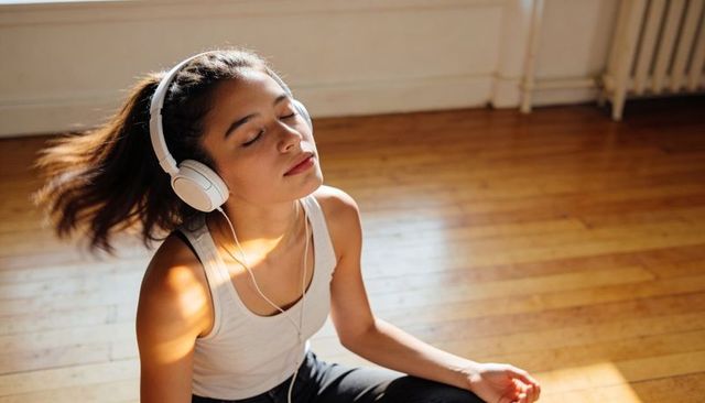 Sunlit woman listening to music with headphones meditating and relaxing on hardwood floor