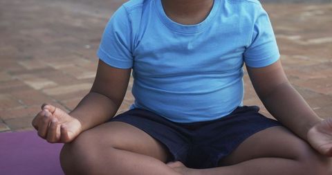 Youth practicing meditation outdoors, hands forming mudra on purple yoga mat