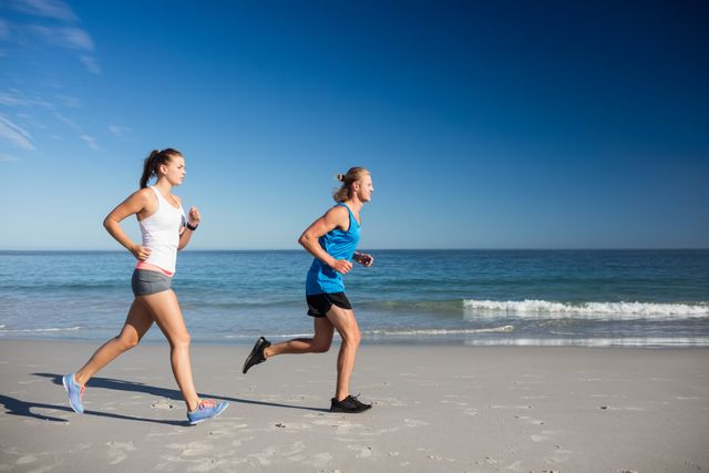 Two friends jogging along a sandy beach with the ocean in the background on a sunny day. Ideal for promoting fitness, healthy lifestyle, outdoor activities, and summer exercise routines. Perfect for use in advertisements, fitness blogs, travel brochures, and wellness campaigns.
