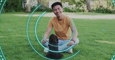 Asian man squatting on lawn playing with small dog, wearable wristband and tech overlay