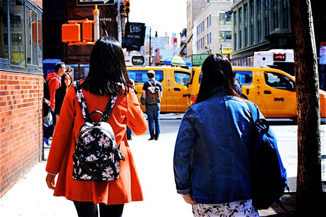 People walking on a busy street in New York City with yellow taxis in the background. This image may be used for visuals related to NYC life, urban environments, public transportation, tourism, and street photography.