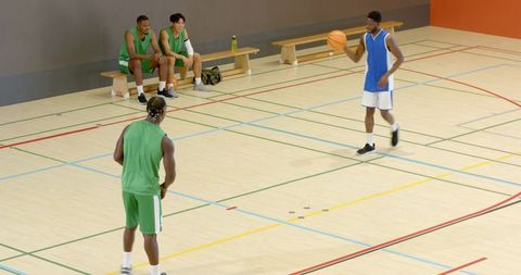 African american basketball players dribbling and guarding during indoor team practice