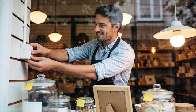 Young barista adjusting wall control in cozy cafe with glass jars and warm lighting