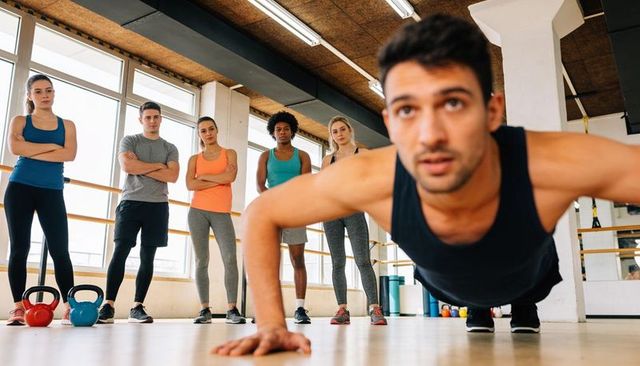 Man performing push-up while group watching in modern gym class with kettlebells and barre